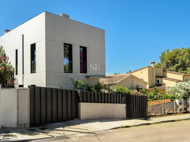 Extérieur d'une maison blanche au design moderne avec une clôture noire sous un ciel bleu clair.