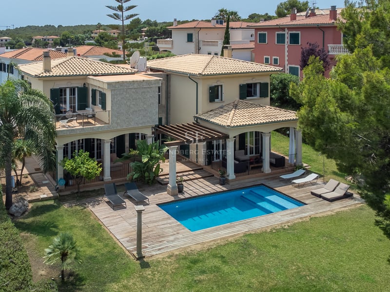 Vue surélevée d'une villa crème avec piscine, terrasse en bois et jardin verdoyant sous le soleil.