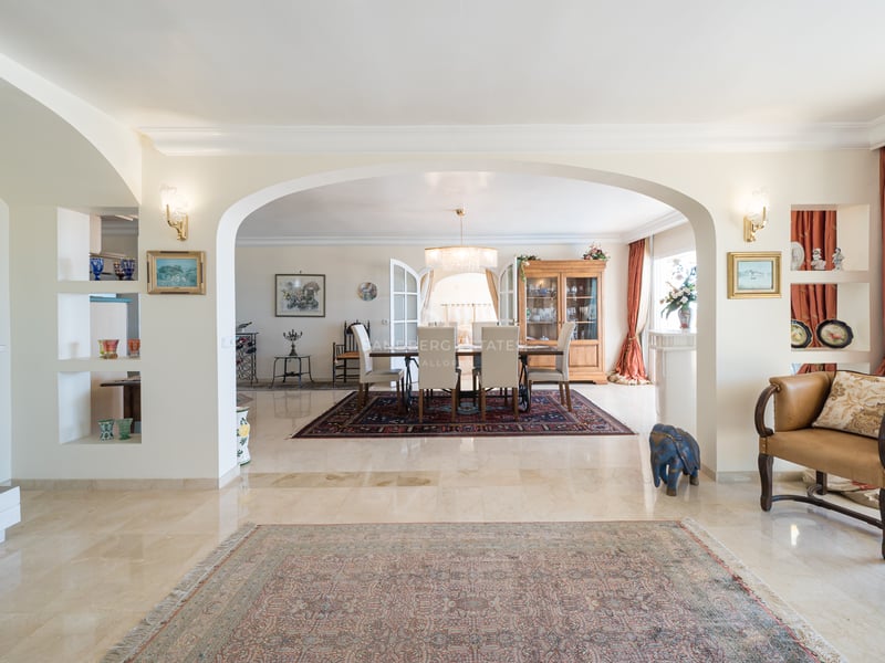 Vaste espace de vie avec sols en marbre et une arche encadrant une salle à manger formelle avec lustre et tapis classiques.