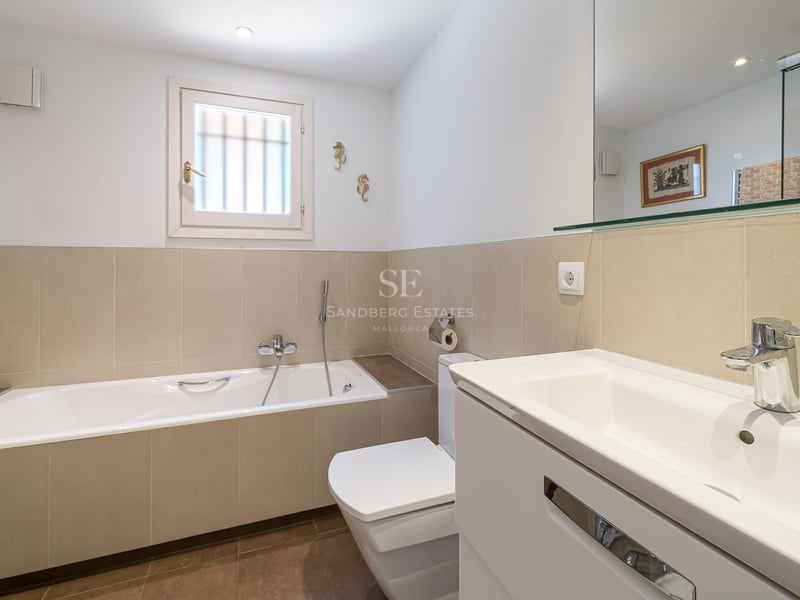 Salle de bain contemporaine avec baignoire encastrée, meuble vasque blanc avec miroir et carrelage beige.