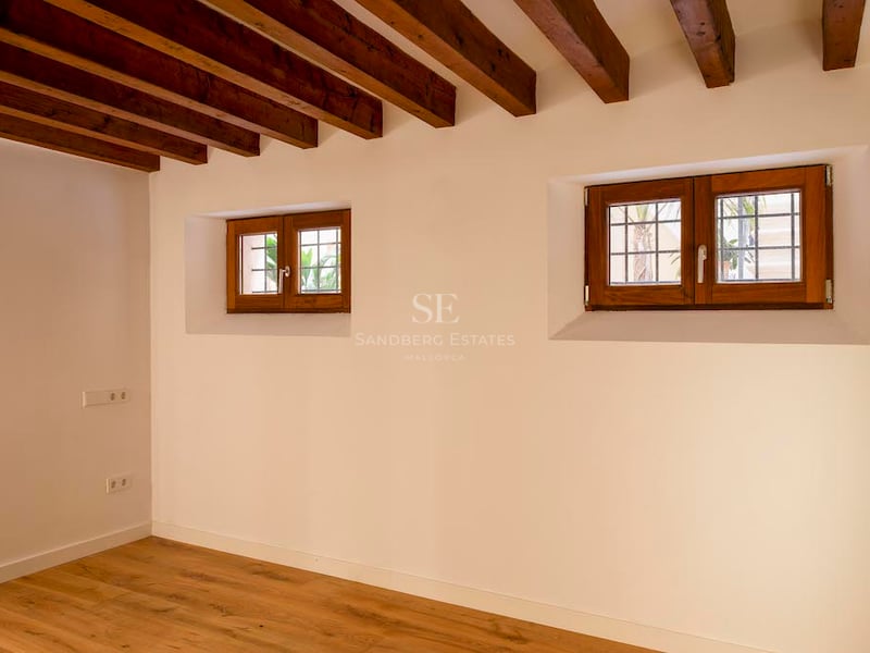 Pièce vide avec plafond à poutres en bois sombre, murs blancs et petites fenêtres en bois.