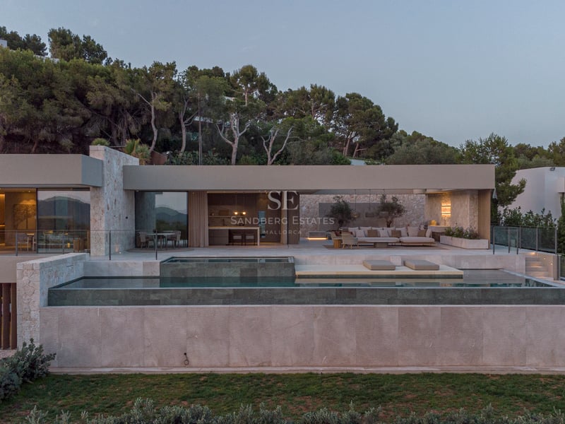 Vue extérieure d'une villa contemporaine avec piscine à débordement multi-niveaux et salon d'été au crépuscule.