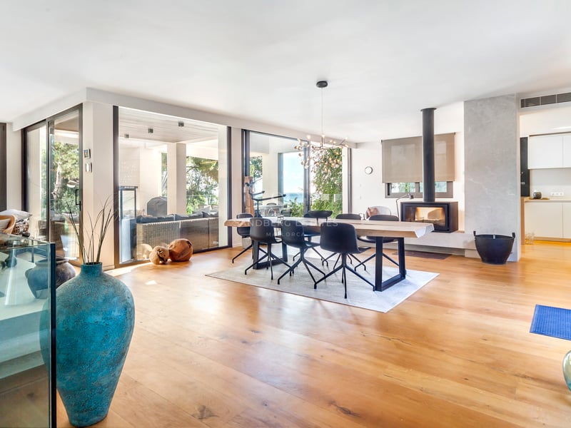 Salle à manger avec table en bois massif, chaises noires modernes, cheminée et baies vitrées ouvrant sur le jardin.