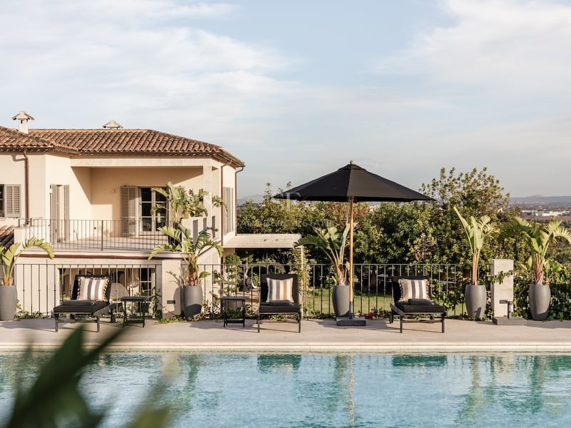 Piscine rectangulaire bordée de bains de soleil noirs, parasol sombre et façade de villa méditerranéenne.