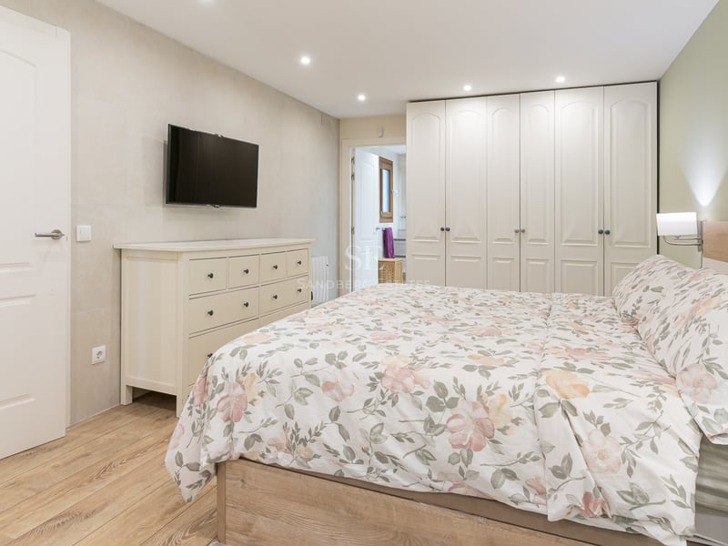 Chambre contemporaine avec lit fleuri, commode blanche, TV murale et grands placards intégrés du sol au plafond.