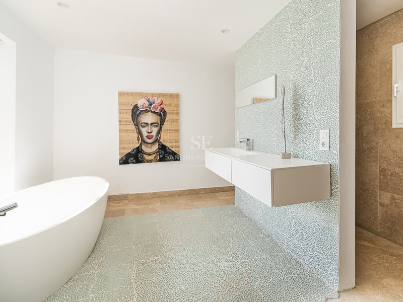 Salle de bain lumineuse avec baignoire ovale, lavabo suspendu, mur en mosaïque bleue et portrait de Frida Kahlo.