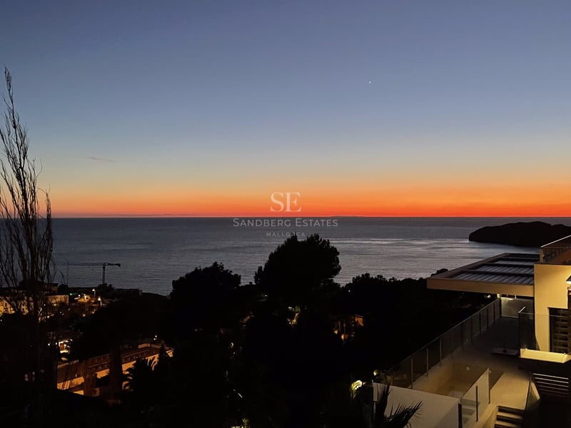 Coucher de soleil sur la mer depuis la terrasse d'une villa moderne avec balustrades en verre et éclairage nocturne.