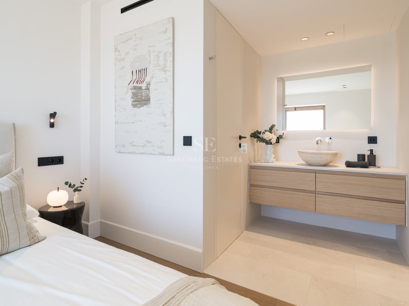 Chambre principale moderne avec lit blanc et meuble vasque flottant en bois avec vasque en pierre et miroir rétroéclairé.