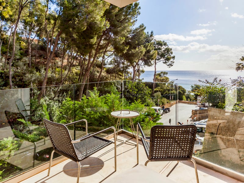 Terrasse avec garde-corps en verre et mobilier moderne donnant sur une pinède et la mer Méditerranée.