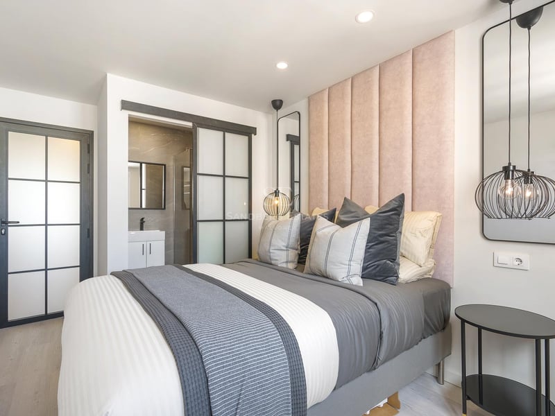 Chambre contemporaine avec tête de lit en velours rose, portes vitrées industrielles et salle d'eau attenante.