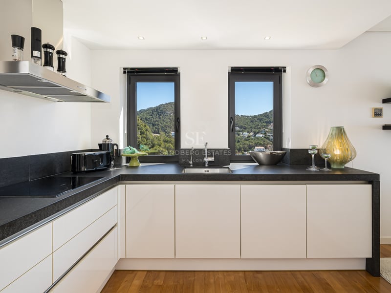 Cuisine blanche contemporaine avec plans de travail en pierre sombre, parquet et fenêtres sur la montagne.