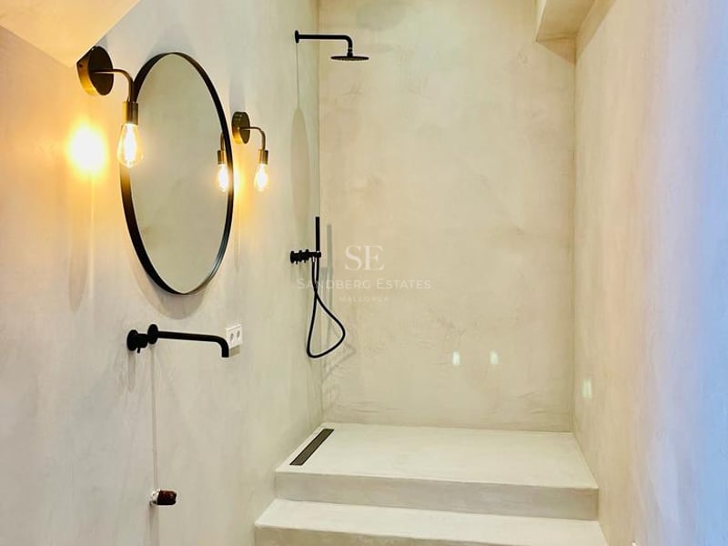 Salle de bain minimaliste avec murs en microciment, sol en terre cuite, vasque en pierre et robinetterie noire mate.