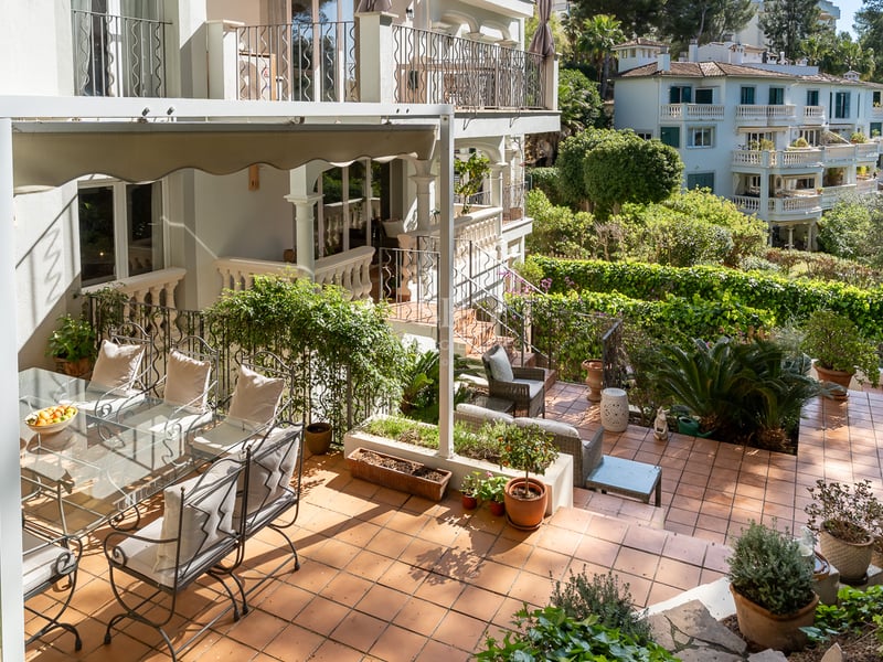 Terrasse méditerranéenne en terre cuite avec mobilier en fer forgé sous un store et jardins luxuriants.