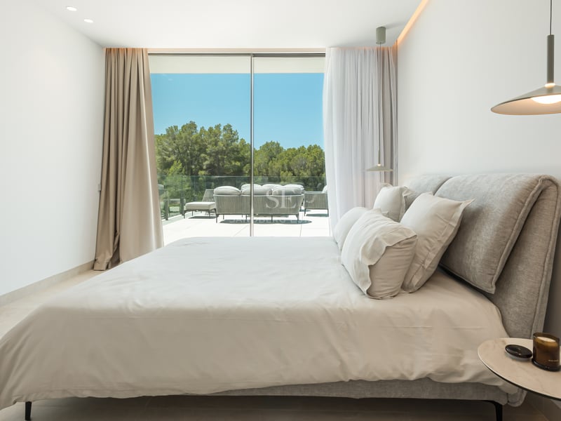 Chambre contemporaine avec grandes baies vitrées ouvrant sur une terrasse avec mobilier et vue sur les arbres.