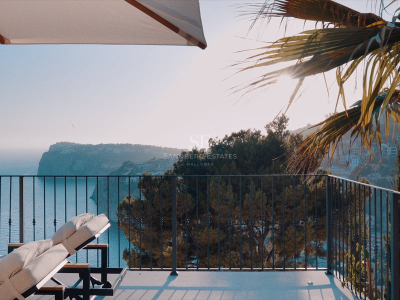Bains de soleil sur une terrasse moderne surplombant une baie côtière avec des falaises et une mer bleue.