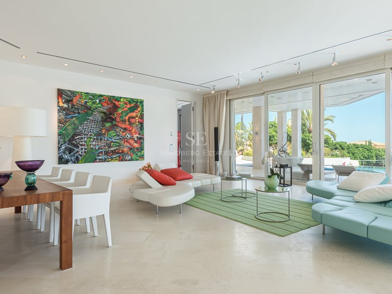Salon lumineux avec baies vitrées ouvrant sur une terrasse, une piscine et une vue dégagée sur la mer.