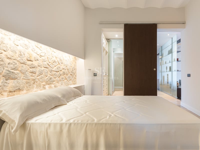 Chambre de luxe avec un grand lit, une tête de lit en pierre naturelle éclairée et une porte coulissante en bois sombre.