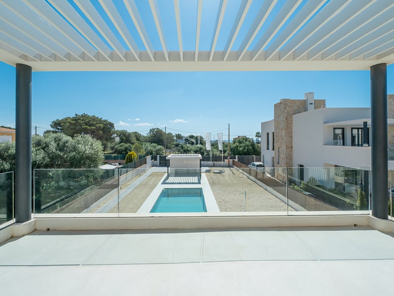 Vue depuis un balcon moderne avec pergola blanche et garde-corps en verre donnant sur une piscine et un jardin.