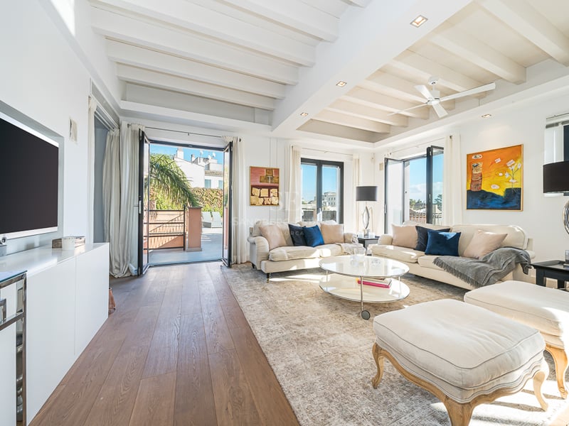 Salon élégant avec canapés crème, plafonds à poutres blanches et accès à une terrasse ensoleillée.