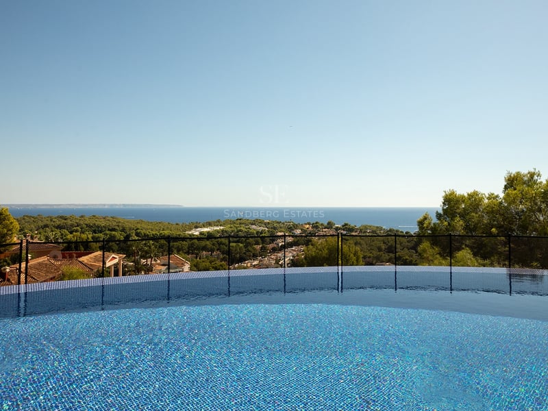 Vue depuis une piscine en mosaïque bleue surplombant la mer Méditerranée et un paysage verdoyant.
