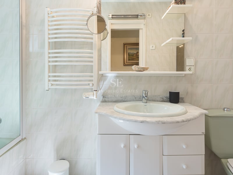 Salle de bains avec meuble blanc, plan en marbre gris, miroir, sèche-serviettes et carrelage mural clair.