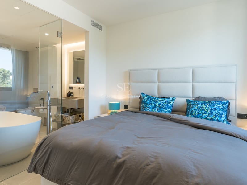 Chambre moderne avec lit gris, lampes turquoise et salle de bain vitrée comprenant une baignoire îlot blanche.