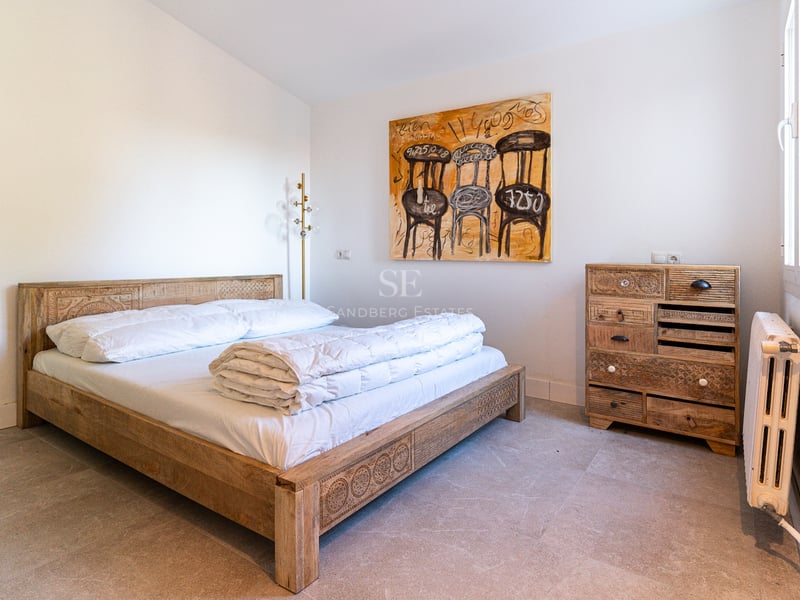 Chambre lumineuse avec lit en bois sculpté, commode assortie, tableau abstrait et sol en pierre naturelle.