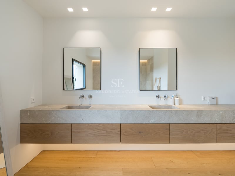Salle de bain moderne avec meuble suspendu en chêne, deux vasques en pierre intégrées et miroirs à cadre noir.