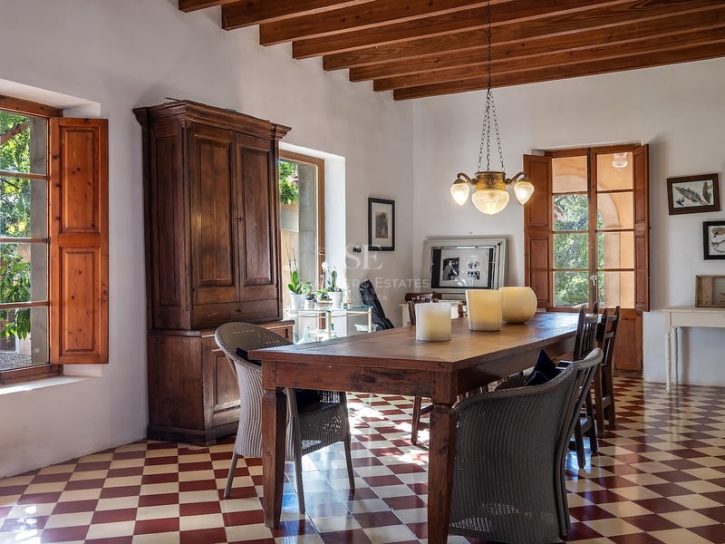Salle à manger rustique avec table en bois, sol en damier rouge et blanc et poutres apparentes.