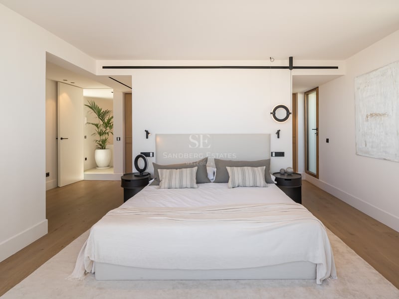 Chambre de maître minimaliste avec grand lit, linge de lit neutre, parquet en chêne et luminaires design noirs.
