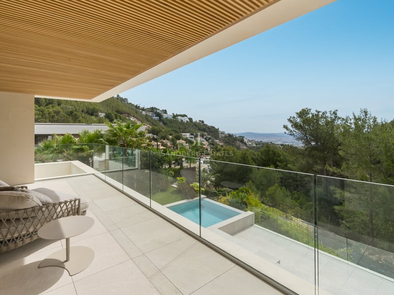 Terrasse moderne avec garde-corps en verre, sol en pierre et plafond en bois, offrant une vue sur la colline et la piscine.
