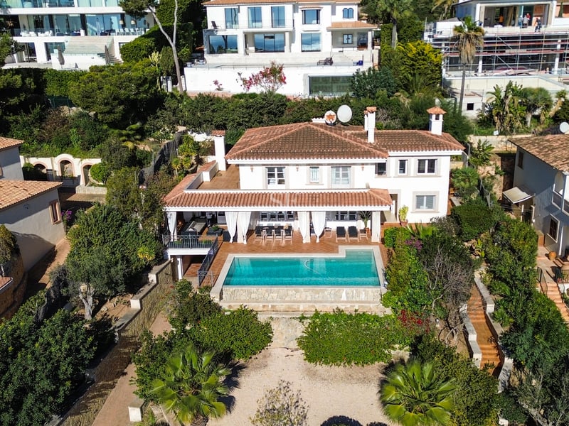 Vue aérienne d'une villa blanche à toit de tuiles avec piscine turquoise et jardins luxuriants.