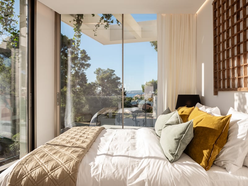 Chambre moderne avec baies vitrées, tête de lit en bois et vue sur les pins et la Méditerranée.