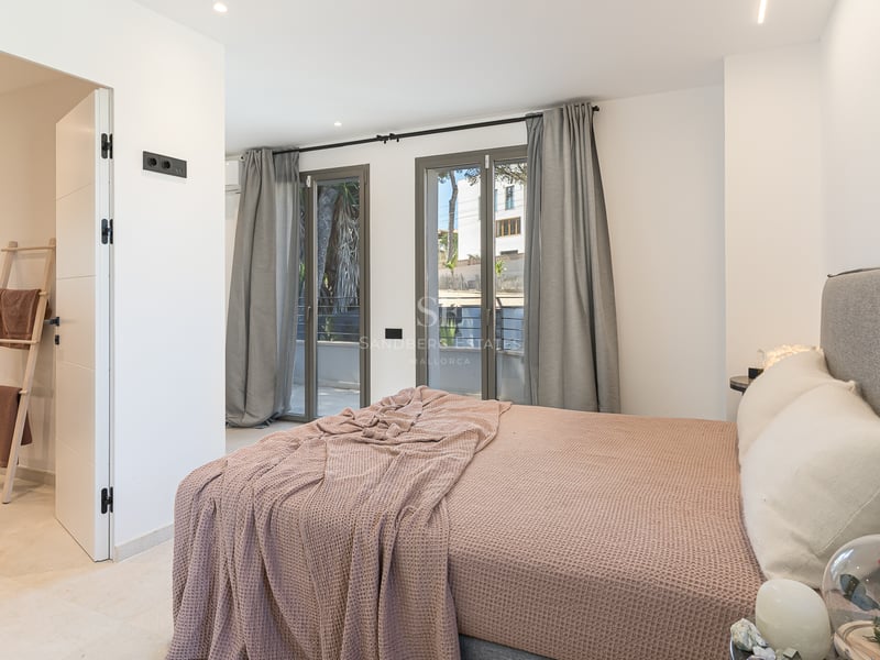Chambre contemporaine avec lit gris, jeté de lit mauve, baies vitrées et accès à une salle de bain attenante.