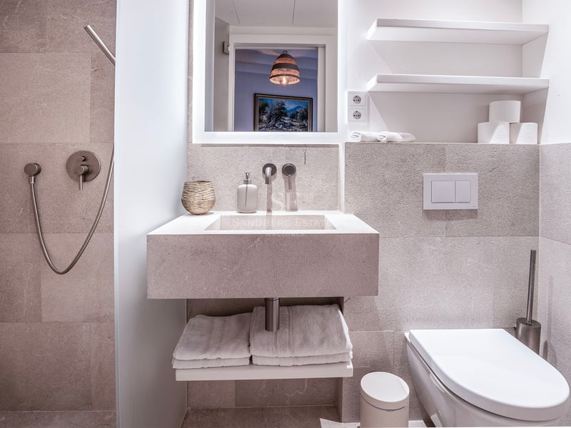 Salle de bain minimaliste avec murs en pierre, lavabo intégré, toilettes suspendues et douche à main chromée.
