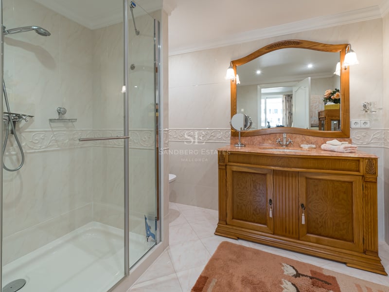 Salle de bain classique avec douche en verre, carrelage en marbre crème et un grand meuble-lavabo en bois sculpté.