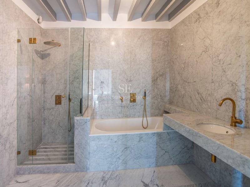 Baño de lujo con paredes de mármol, ducha de cristal, bañera integrada y elegantes grifos de latón.