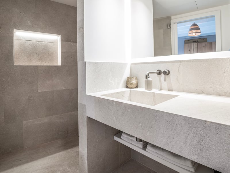 Salle de bain moderne en pierre avec vasque intégrée, robinet mural et niche murale éclairée.