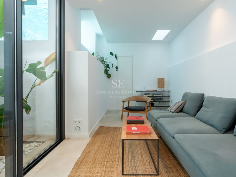 Salon moderne avec canapé bleu, table basse en bois, tapis en jute et baie vitrée donnant sur des plantes tropicales.