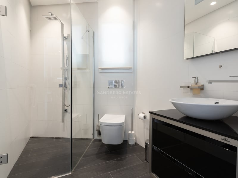 Salle de bain contemporaine avec carrelage blanc, douche en verre, toilettes suspendues et vasque sur meuble noir.