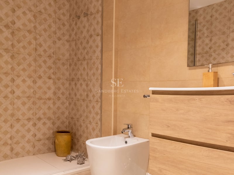 Salle de bain contemporaine avec carrelage tons sable, douche à l'italienne, meuble vasque en bois et bidet blanc.