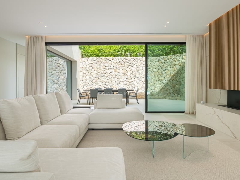 Salon contemporain élégant avec grand canapé blanc, cheminée en marbre et baies vitrées ouvrant sur un patio en pierre.