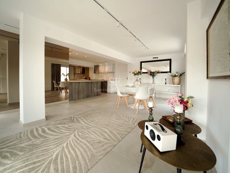 Intérieur lumineux à aire ouverte avec salle à manger blanche, îlot de cuisine en bois et carrelage de couleur sable.