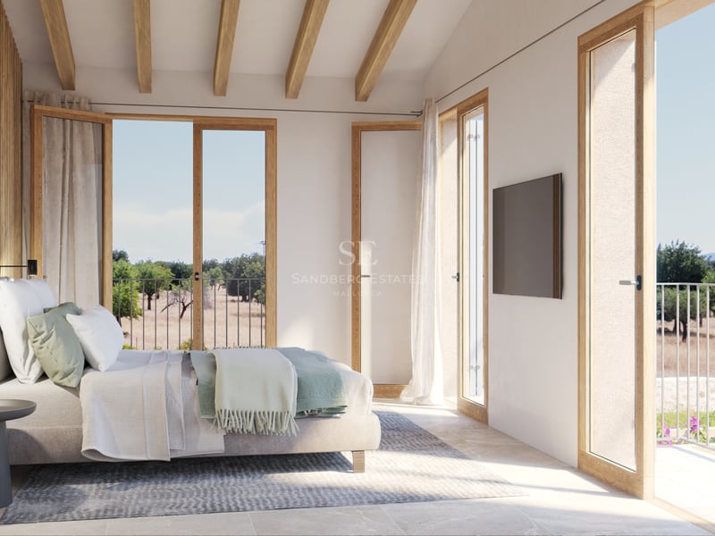 Chambre principale lumineuse avec poutres en bois, sol en pierre et portes-fenêtres ouvrant sur la nature.