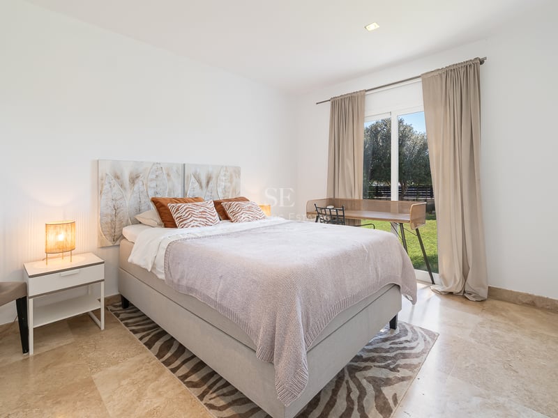 Chambre moderne avec sol en marbre, lit double et porte vitrée ouvrant sur un jardin verdoyant.