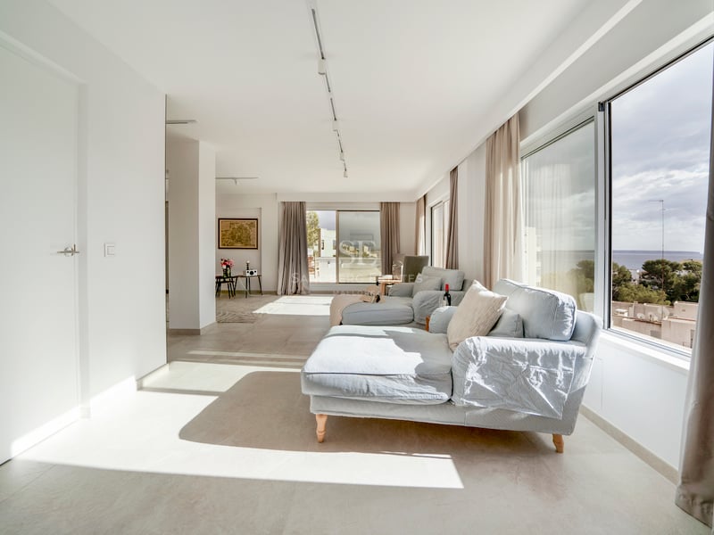 Salon moderne avec canapés à rayures bleu clair et grandes baies vitrées offrant une vue sur la mer et la côte.