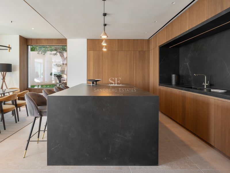 Cuisine moderne avec un grand îlot en pierre noire, des meubles en chêne cannelé et des luminaires suspendus.