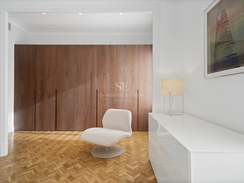 Espace dressing minimaliste avec placards en bois, parquet à chevrons et fauteuil design blanc.