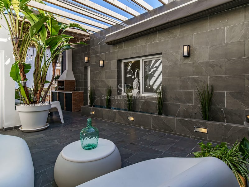 Patio de luxe avec murs en pierre grise, mobilier moderne blanc, pergola en bois et plantes tropicales.