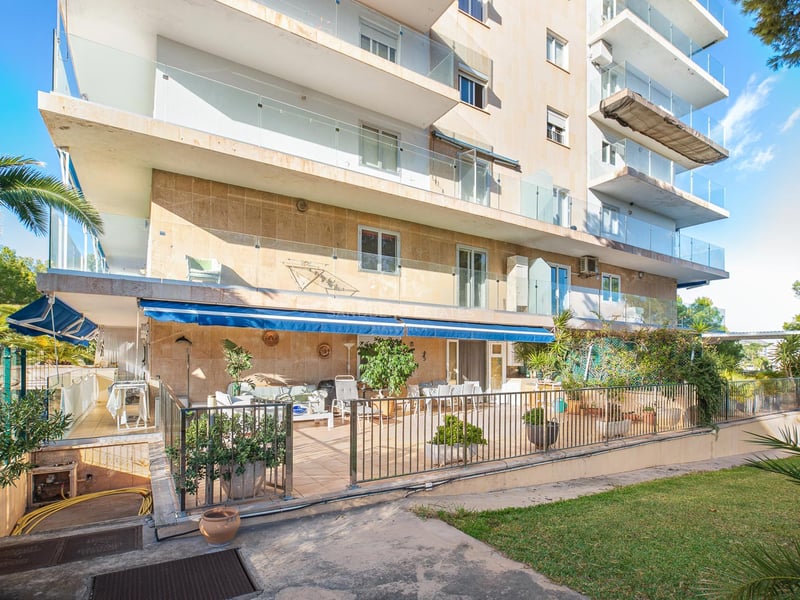 Immeuble d'appartements avec parement en pierre, balcons en verre et grande terrasse au rez-de-chaussée.
